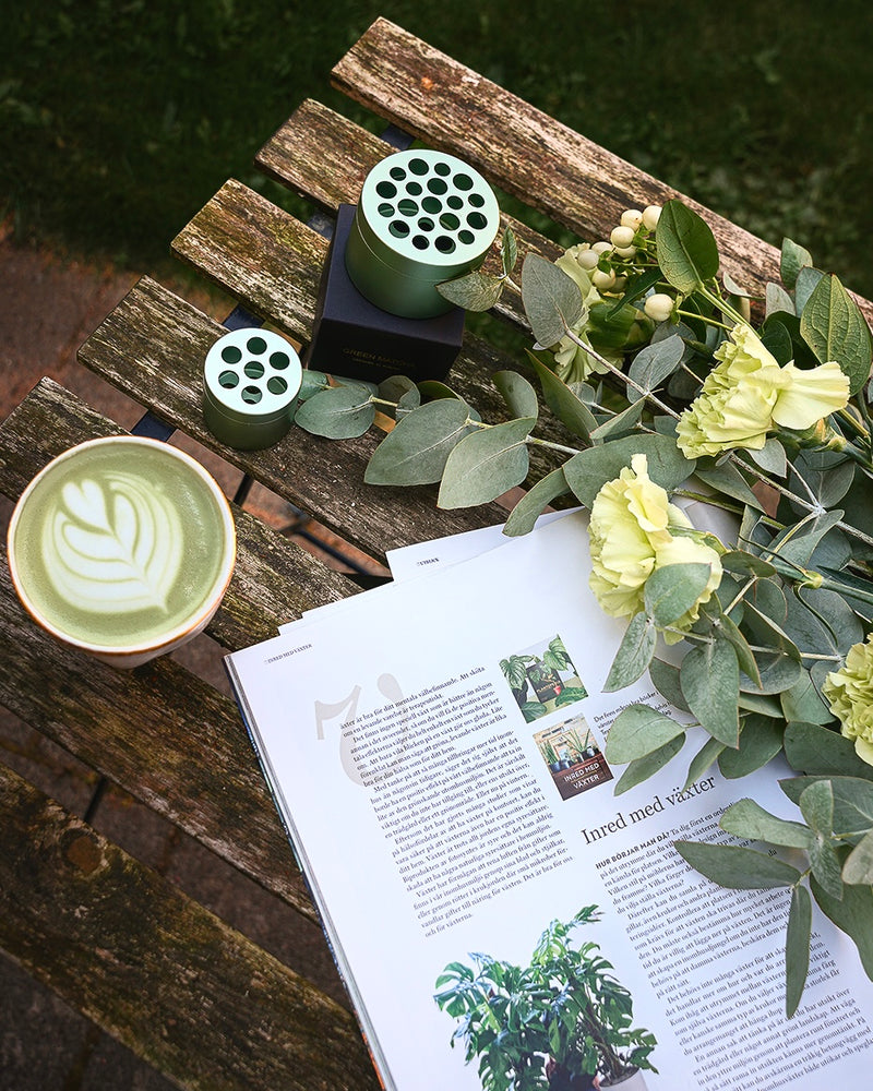 Eucalipto e una tazza di tè matcha accanto all'attrezzo per la composizione di bouquet Hanataba su un tavolo di legno in un giardino.