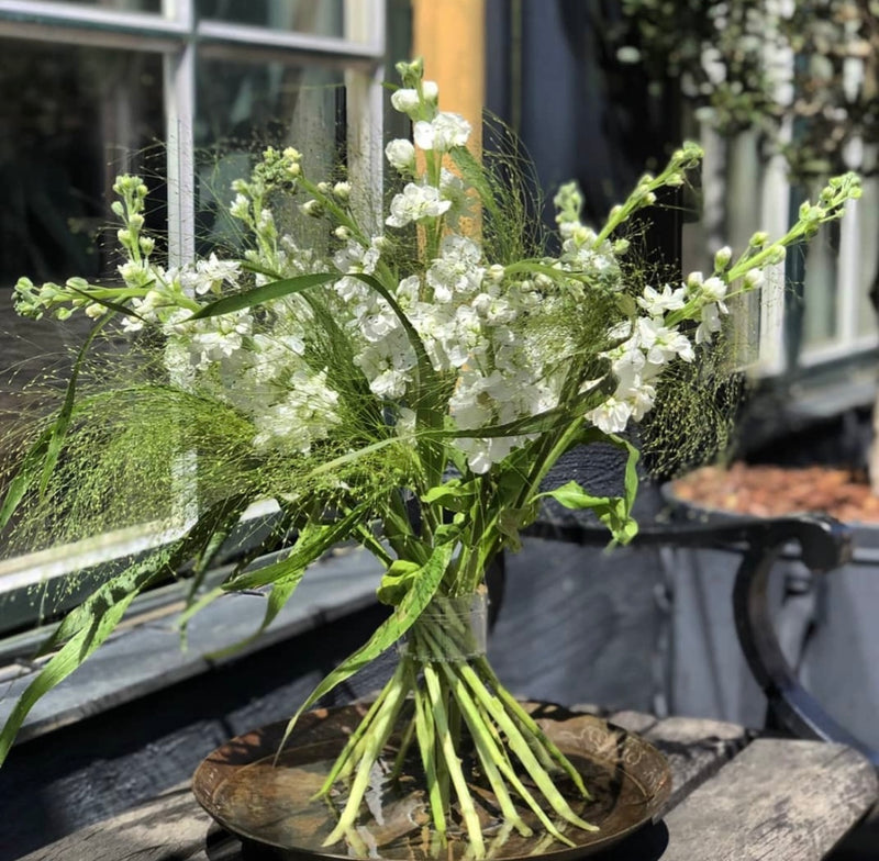 Una composizione Ikebana con un assortimento di delicati fiori bianchi, completata da un porta stelo a spirale in cristallo trasparente Hanataba per un tocco moderno.