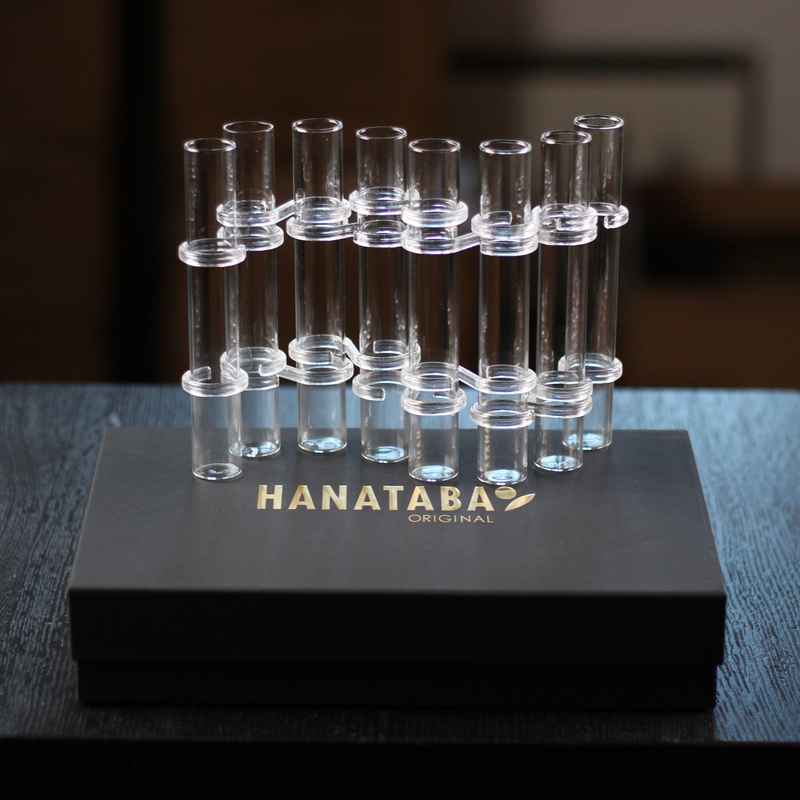 Un set di flute Hanataba Original Flower, esposto in un'elegante scatola nera con marchio in oro, con una collezione di tubi di vetro trasparenti progettati per creare creativi allestimenti floreali.