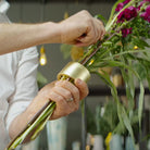 Le mani di un uomo montano abilmente una vivace composizione floreale utilizzando un Hanataba Champagne Gold.