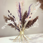 Un bouquet Hanataba Champagne Gold con fogliame viola, nero e bianco su uno sfondo neutro, per un'eleganza moderna.