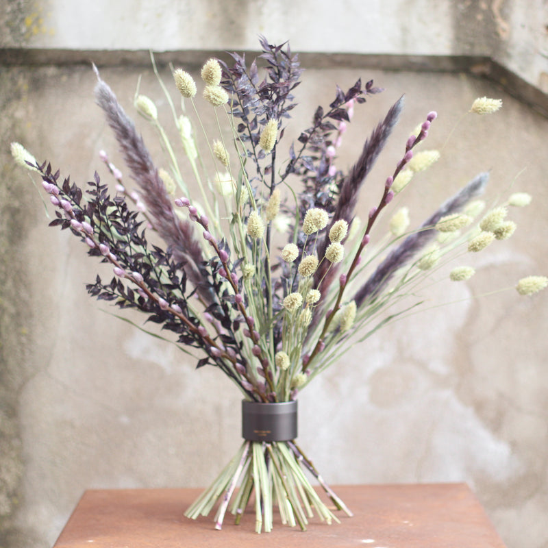 Un bouquet di fogliame viola scuro e fiori verde chiaro fissato con un twister Hanataba Pitch Black su una superficie di legno.